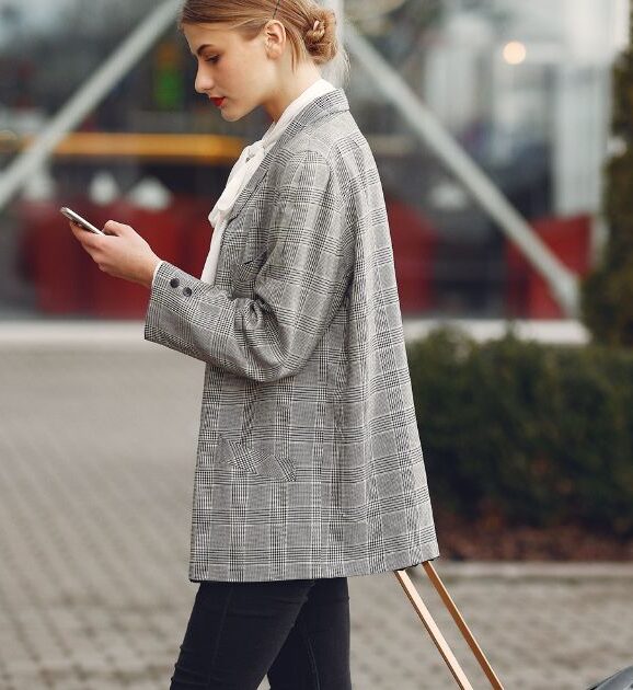 Traveler checking her phone while pulling a suitcase outside an airport