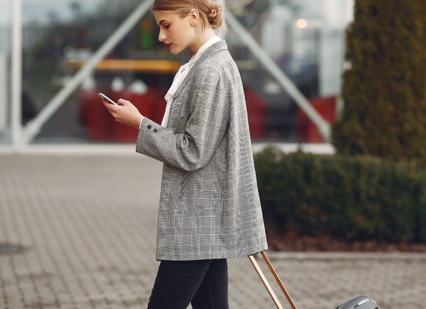 Traveler checking her phone while pulling a suitcase outside an airport
