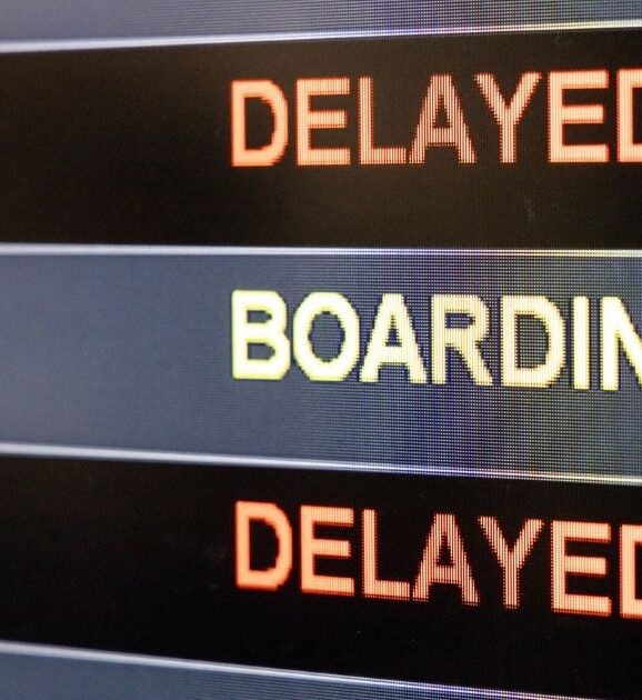 Airport departure board displaying boarding and delayed flight statuses