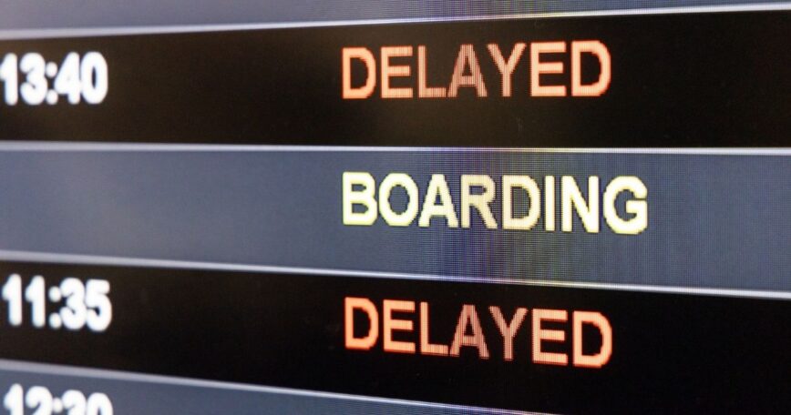 Airport departure board displaying boarding and delayed flight statuses