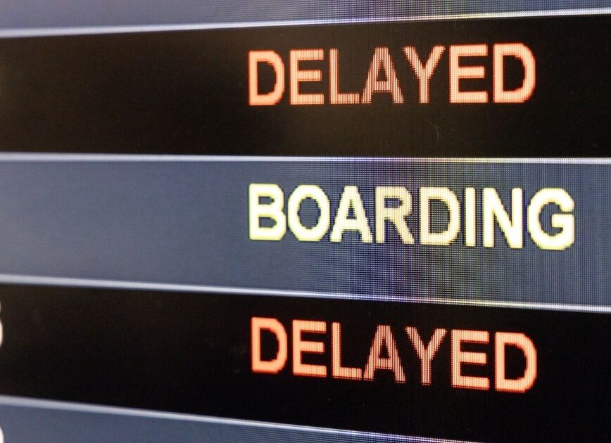 Airport departure board displaying boarding and delayed flight statuses